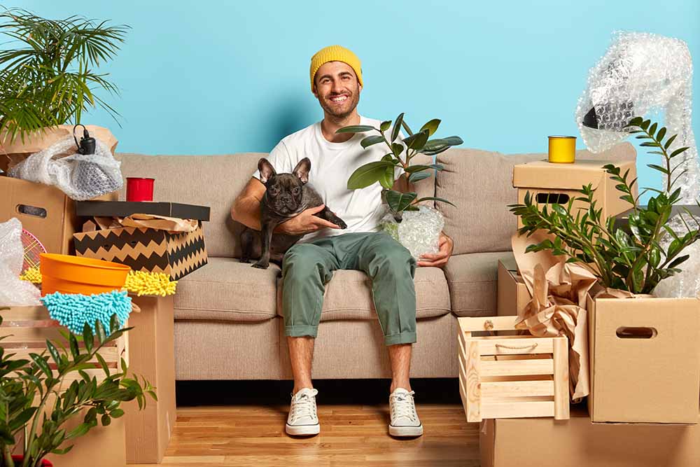 Un jeune homme dans son appartement est assis sur un sofa avec son chien